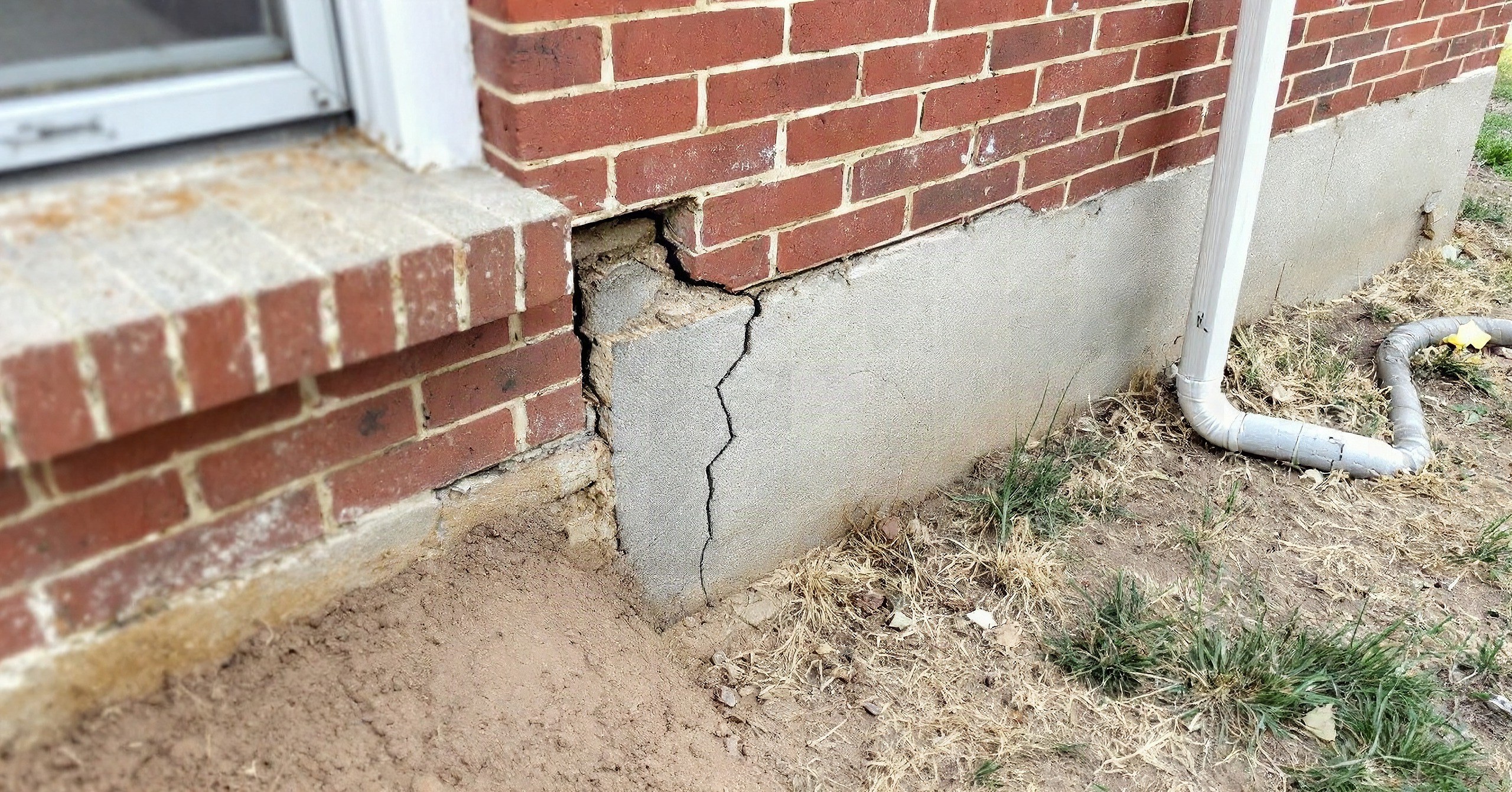 Illustrative example: the foundation corner of a Tulsa brick home before repair, a crack through the concrete stem wall, brick pulled out of line and soil piled against it